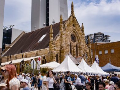 Attendees of the Greek Street Fair Burwood in the foreground with stalls set up and the St Nectarios Church in the background