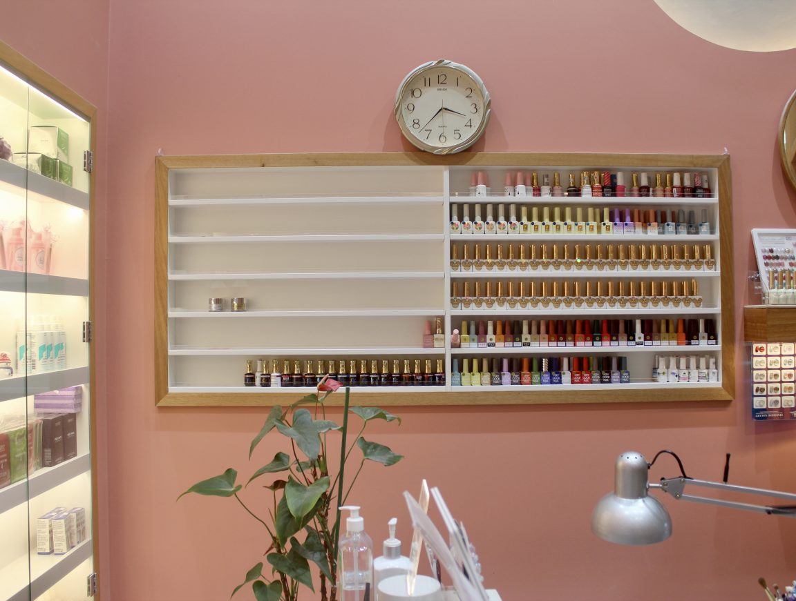 The interior of a nail salon, replete with many bottles of colourful nail poliish bottles in a cabinet against a pink pastel wall.
