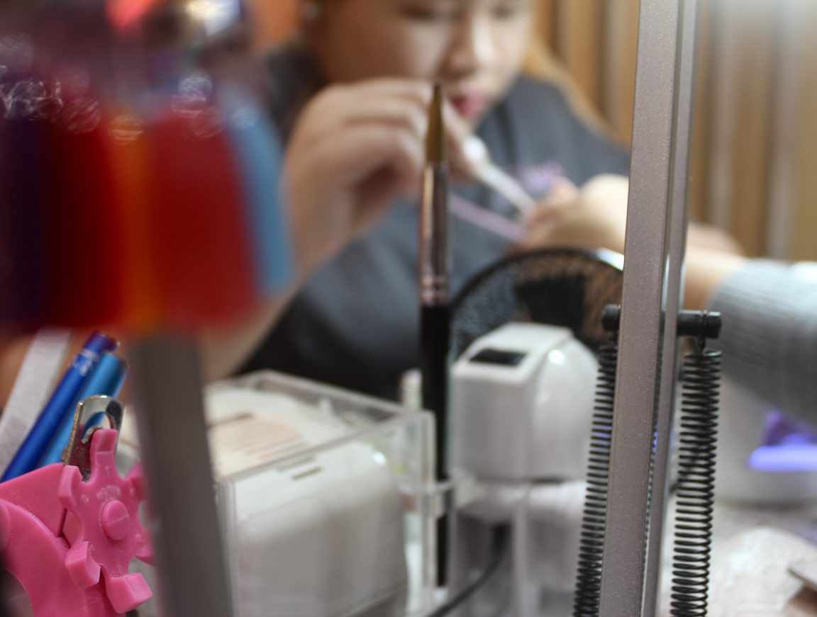 A close up image of manicure tools with an out of focus nail technician in the background